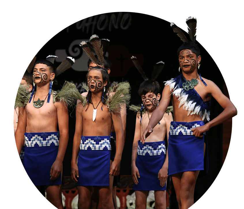 Young tamariki perform Kapa Haka on stage, proudly wearing custom-knitted blue and white Tātua and Maro made by Kapa Haka Makers.
