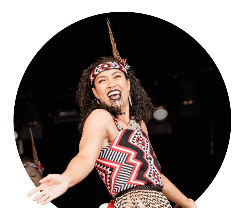 A happy wahine performs Kapa Haka on stage, adorned in a custom-knitted kākahu made by Kapa Haka Makers Aotearoa.